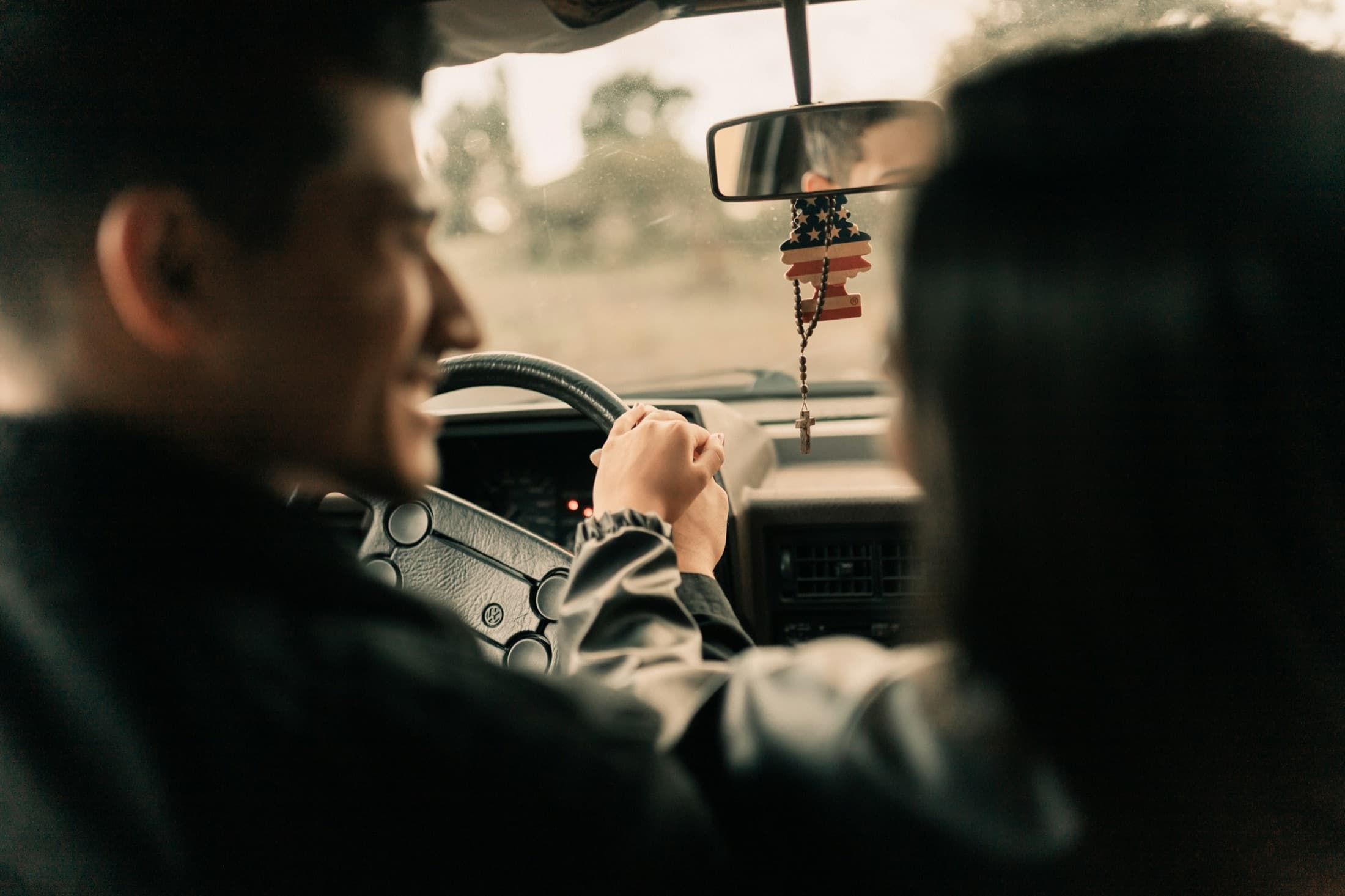 Asian couple holding hands while driving, view from the back seat at golden hour