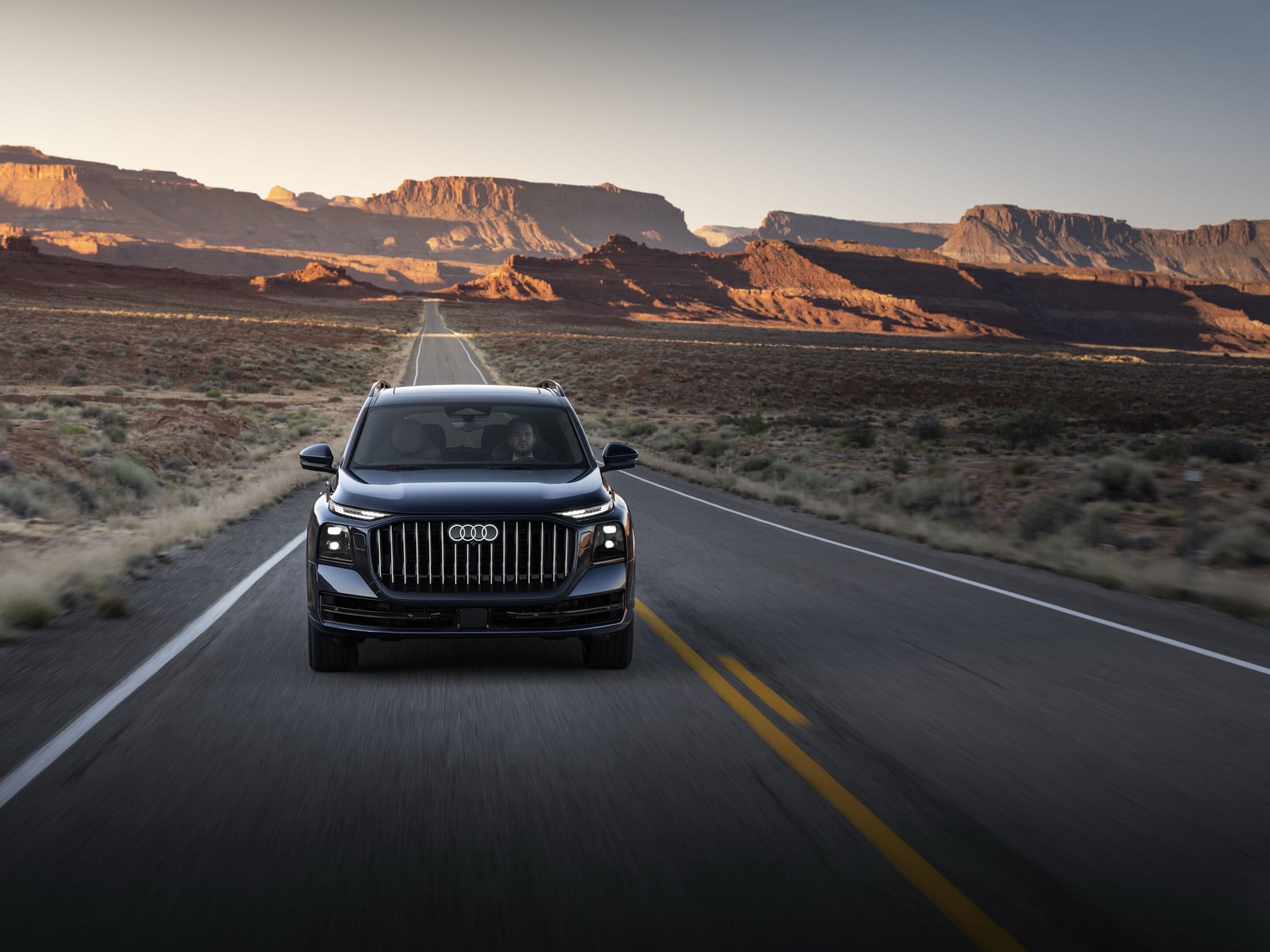 2027 Audi Q9 driving toward the camera on a desert highway at golden hour