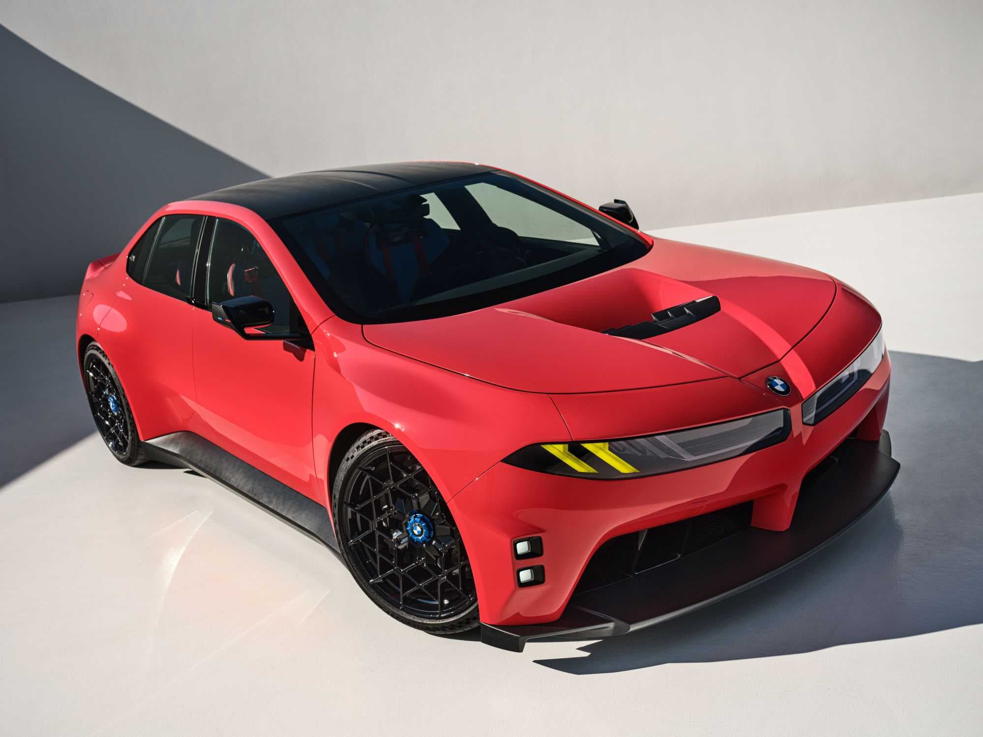BMW M Concept Neue Klasse in Monza Red, front three-quarter outdoor studio view with yellow M light signature and black roof