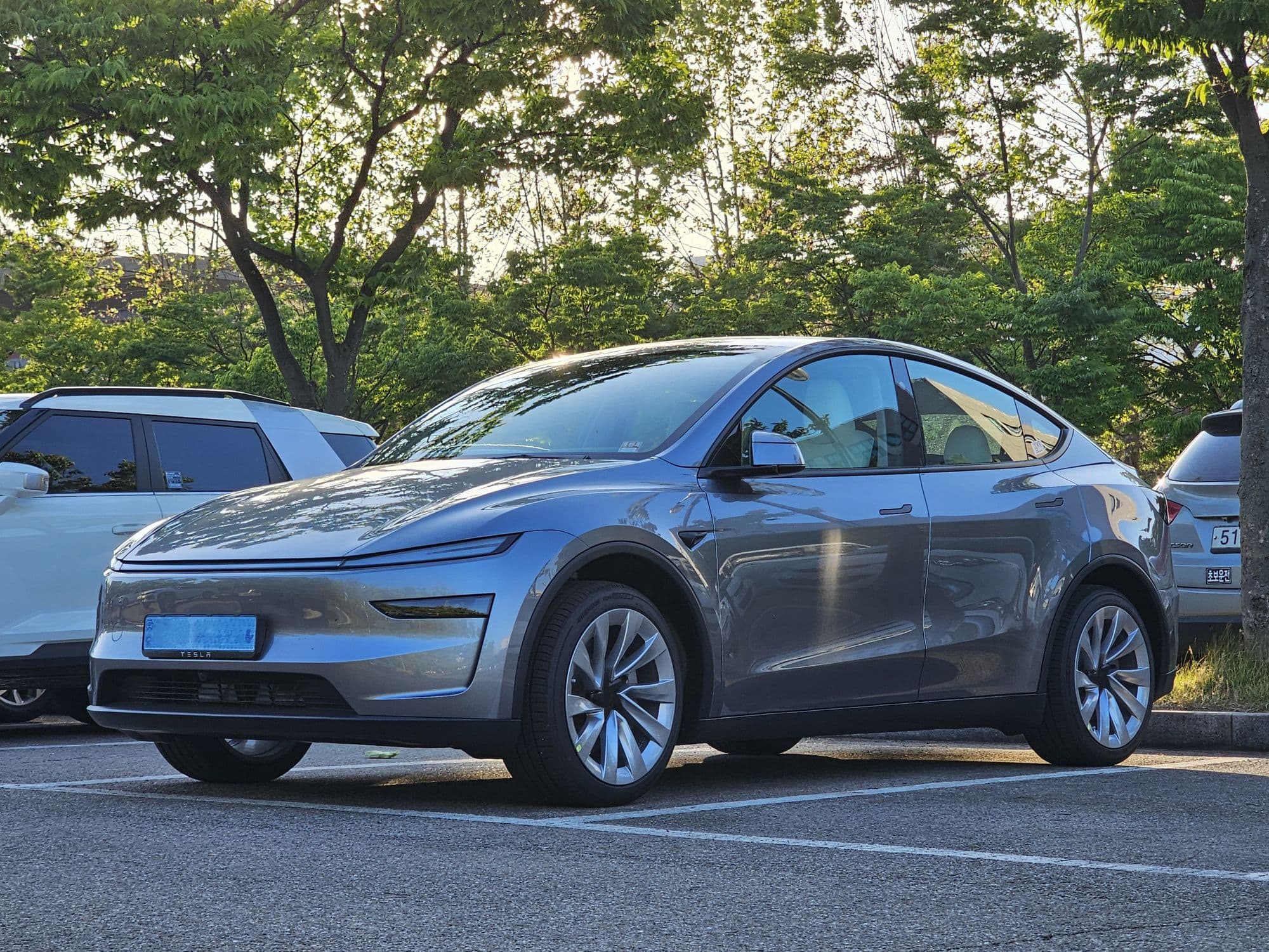 Silver Tesla Model Y with flush door handles parked outdoors at golden hour
