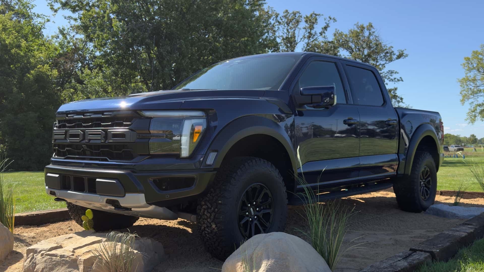 Dark blue Ford F-150 Raptor on a sand display, front three-quarter view