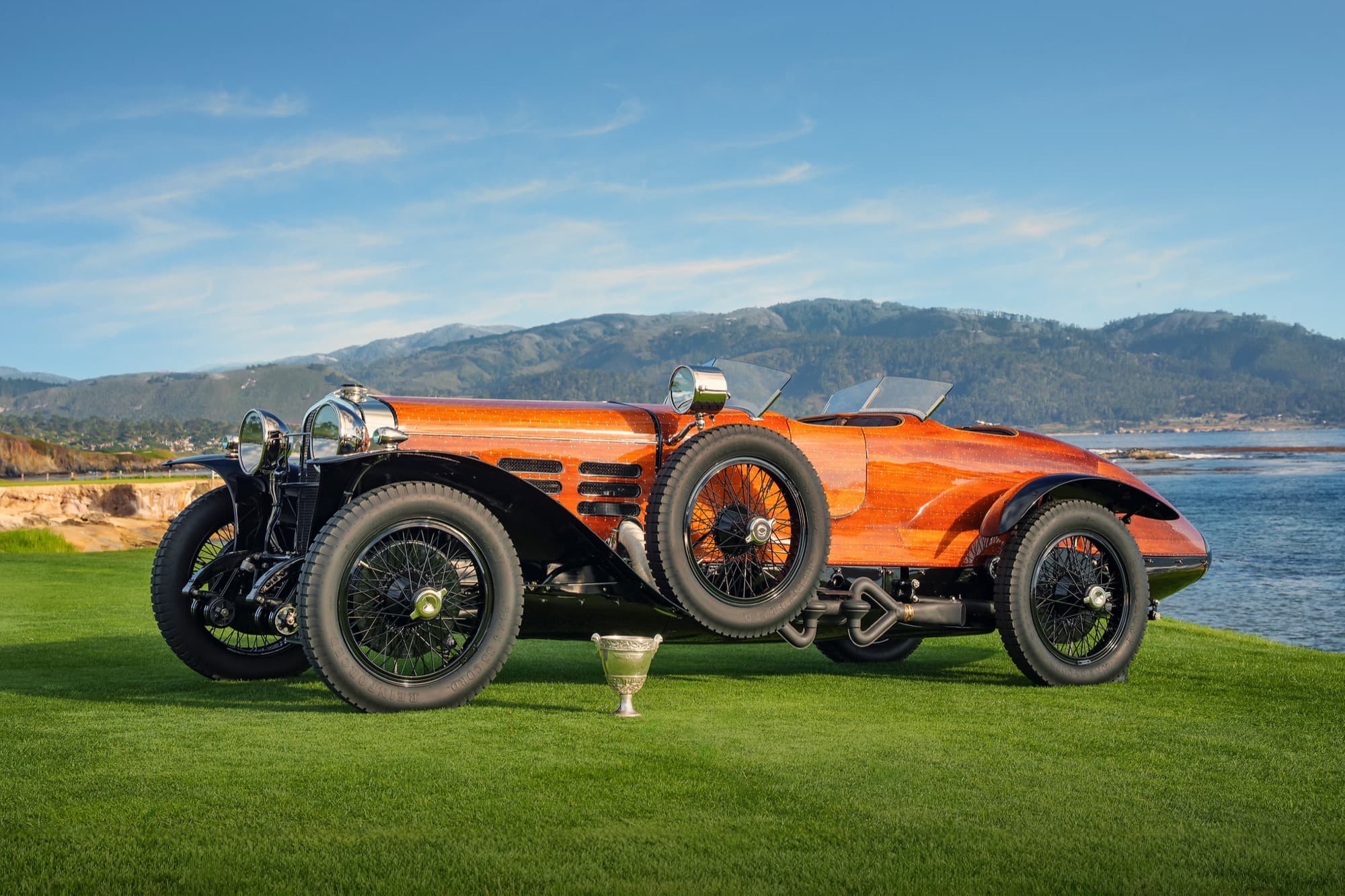 1924 Hispano-Suiza H6C Tulipwood Torpedo in mahogany boat-tail bodywork parked on the Pebble Beach lawn with a silver Best of Show trophy in front