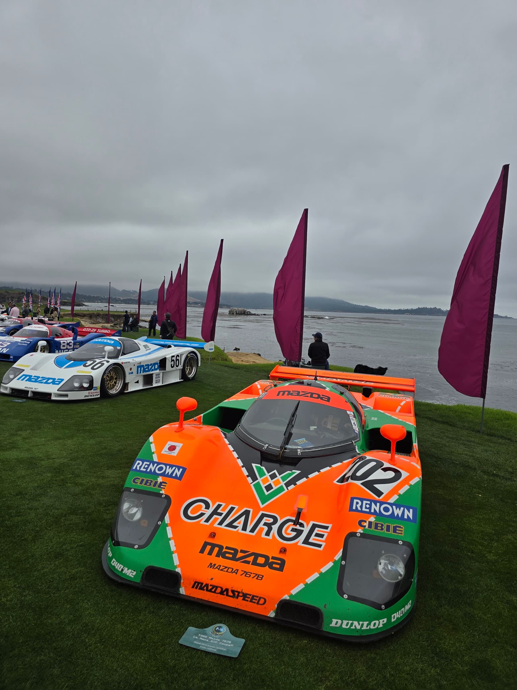 Charge Renown Mazda 767B and other Japanese endurance race cars on the Pebble Beach Concours lawn beside Carmel Bay
