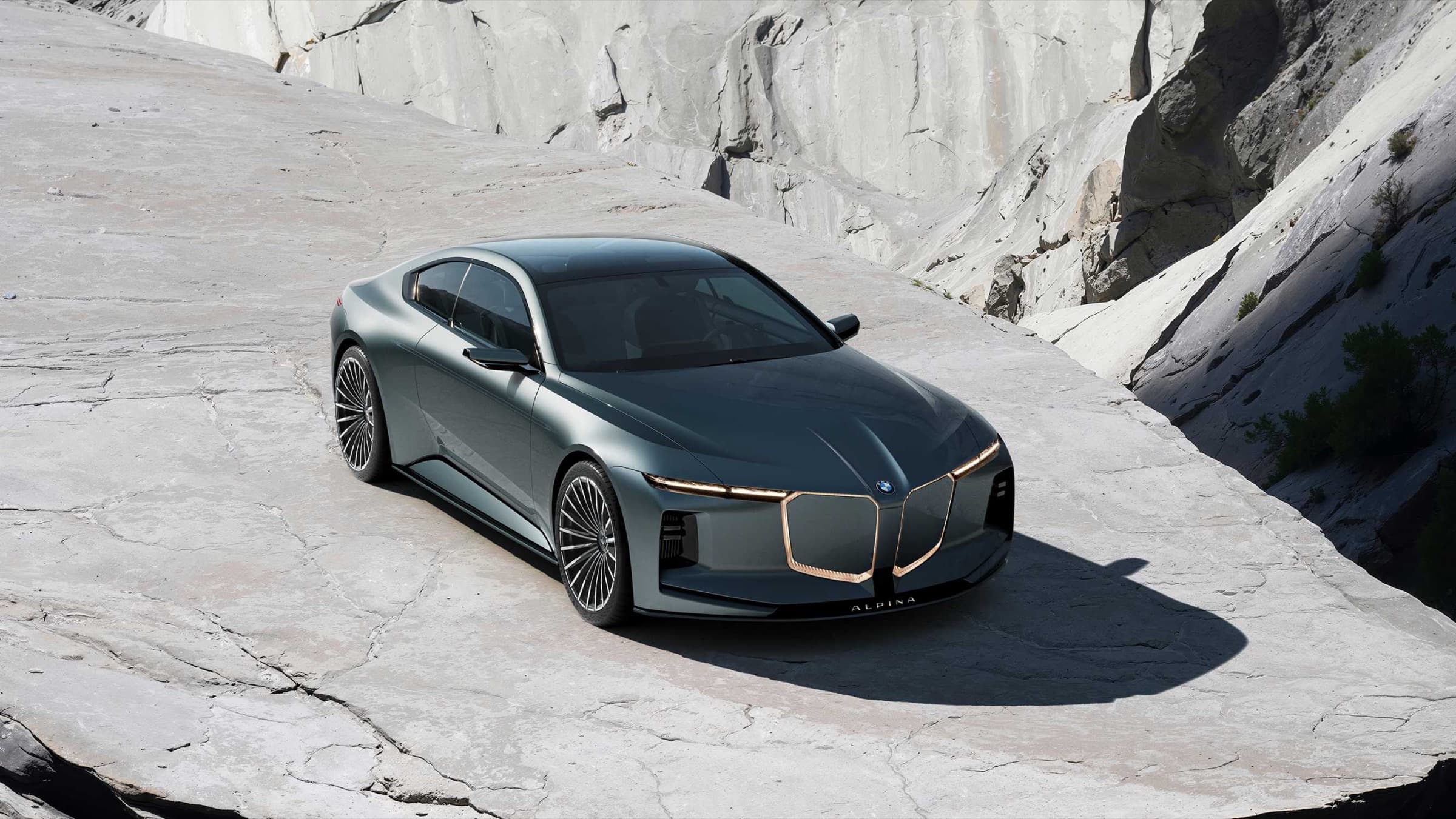 Vision BMW ALPINA concept coupe in metallic sage green, front three-quarter view on pale rock with shark-nose kidneys, ALPINA lettering on the splitter, and classic multi-spoke wheels