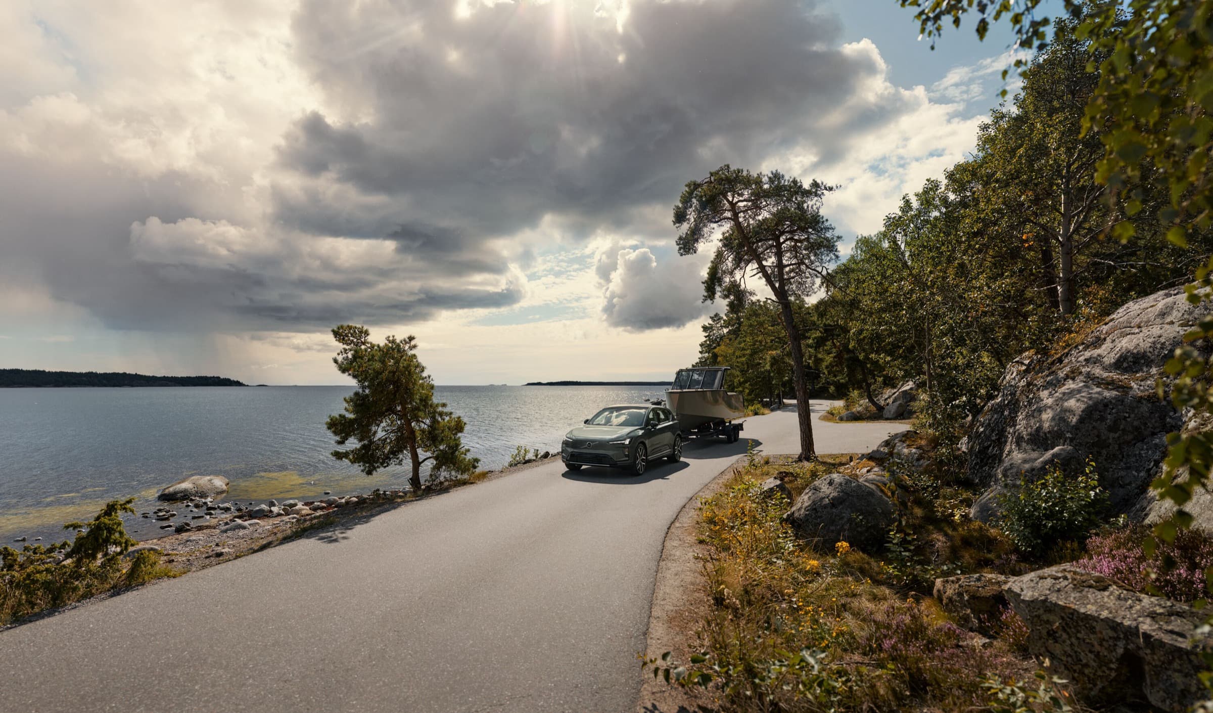Volvo EX60 towing a boat beside a rocky coastline