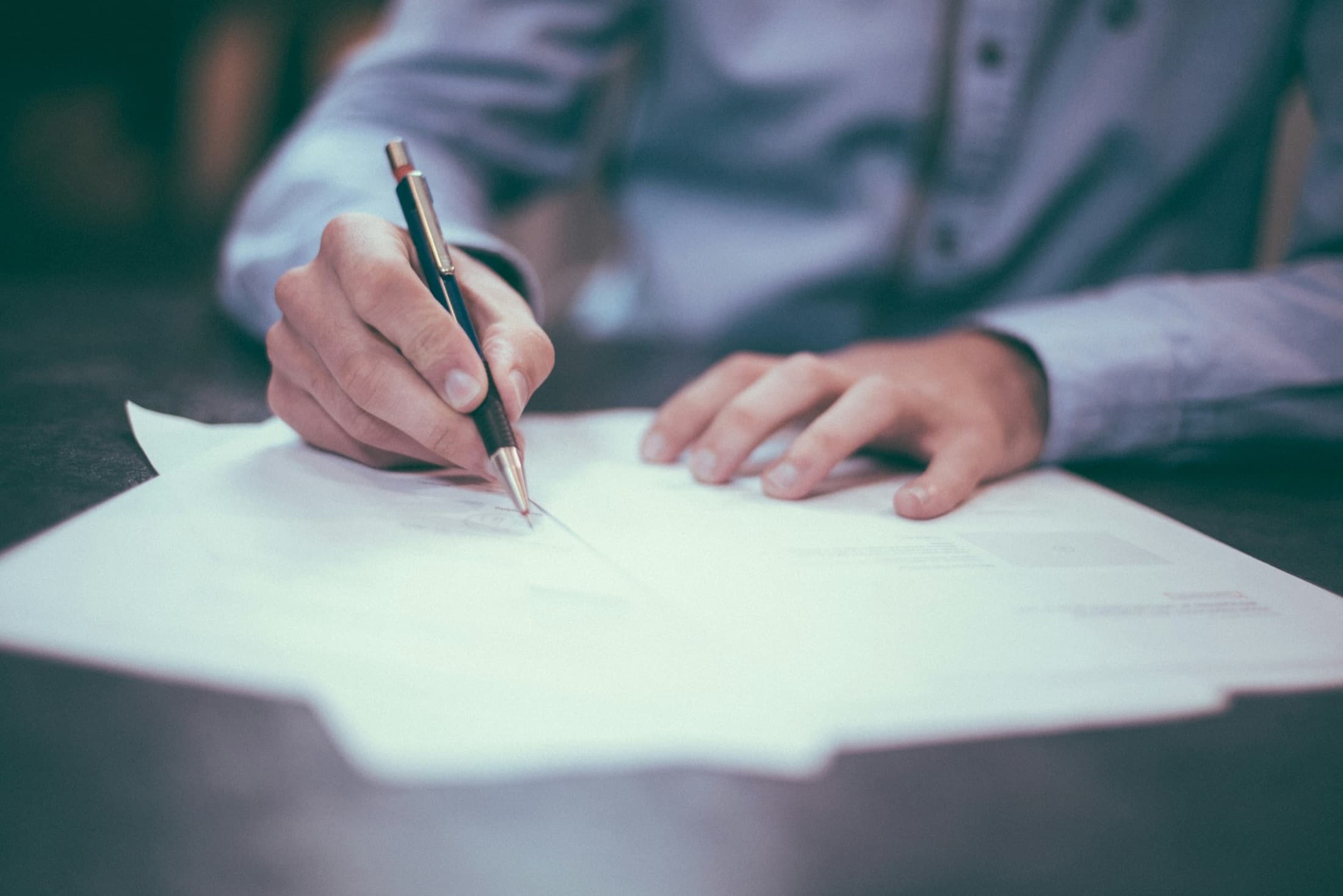 Hands writing notes on paper at a desk while reviewing documents