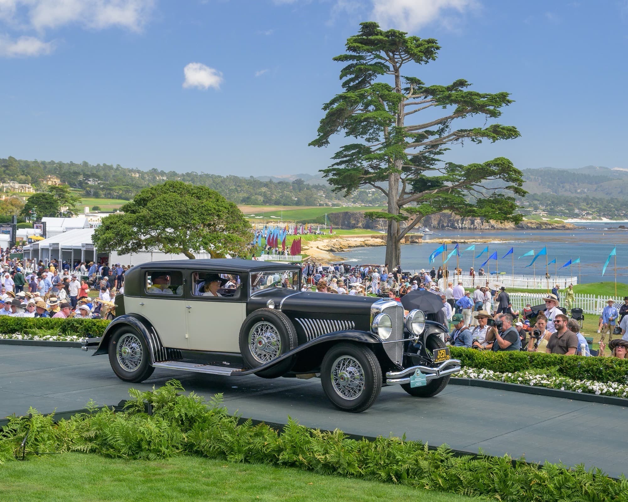 Prewar classic on the Pebble Beach Concours awards ramp with Monterey cypress, spectators, and Pacific coastline