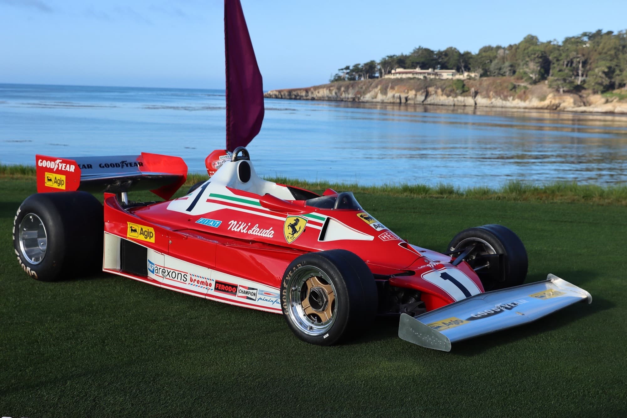 Historic Ferrari Formula One car on the Pebble Beach lawn with Stillwater Cove and the Monterey Peninsula coastline behind